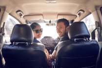 Улыбающаяся молодая пара в машине смотрит в камеру — стоковое фото