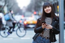 Jeune attrayant asiatique femme en ville en utilisant smartphone — Photo de stock