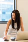 Молода красива азіатська жінка працює з ноутбуком і калькулятором в сучасному офісі — стокове фото
