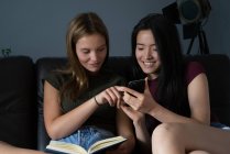 Chinesin schaut mit blonder Freundin aufs Smartphone. — Stockfoto