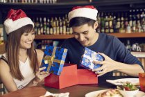 Happy young asian couple celebrating christmas together in cafe and sharing gifts — Stock Photo