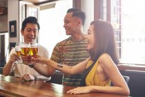 Happy young asian friends together in bar having beer — Stock Photo