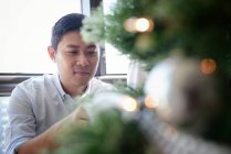 Happy young asian man decorating fir tree — Stock Photo