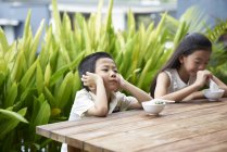 Happy asian siblings sitting at wooden table — Stock Photo