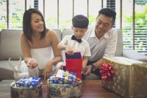 Mère et père regardent leur fils ouvrir ses cadeaux de Noël dans leur maison à Singapour . — Photo de stock
