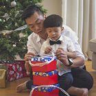 Pai e filho sentam-se no chão e abrem presentes de Natal — Fotografia de Stock