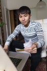 Young adult asian man holding cash and using laptop — Stock Photo