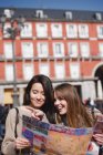 Two beautiful female friends walking in city with map and pointing — Stock Photo
