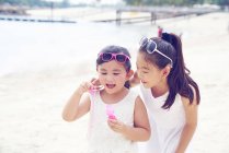 Две младшие сестры проводят время вместе на пляже и пускают пузыри — стоковое фото