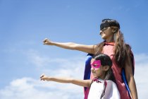 Young asian mother with cute daughter in superhero costumes posing against blue sky — Stock Photo
