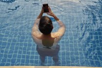 Jovem usando telefone na piscina — Fotografia de Stock