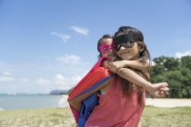 Молодая азиатская мать с симпатичной дочерью в костюмах супергероя позирует на фоне голубого неба — стоковое фото