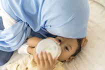 Jovem asiático muçulmano mãe e filho, mãe alimentação bebê com leite garrafa — Fotografia de Stock