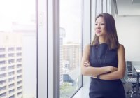 Jovem asiático mulher de negócios olhando para fora janela no moderno escritório — Fotografia de Stock