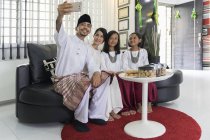 Feliz asiático família celebrando hari raya em casa e tomando selfie — Fotografia de Stock