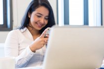 Молода жінка посміхається на мобільний телефон в сучасному офісі — стокове фото