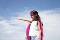 Young little cute asian girl posing in superhero costume against blue sky — Stock Photo