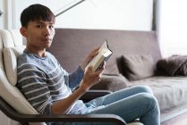 Young adult asian man reading book at home — Stock Photo