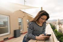 Young asian business woman using smartphone on balcony — Stock Photo