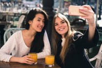 Дві красиві жінки-друзі беруть селфі на смартфон у кафе — стокове фото