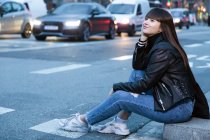 Joven atractivo asiático mujer en ciudad sentado cerca de road - foto de stock