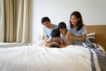 Счастливая молодая азиатская семья вместе в спальне чтение книги — стоковое фото