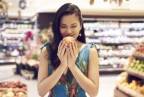 Молодая красивая азиатка, нюхающая яблоко в магазине — стоковое фото