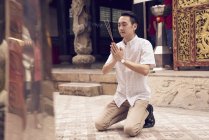 Junger asiatischer Mann betet im Tempel mit Stöcken — Stockfoto