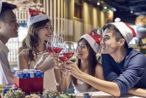 Happy young asian friends celebrating christmas together in cafe and cheering wine — Stock Photo