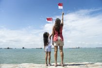 Rear view of young asian mother with cute daughter rising Singaporean flags — Stock Photo