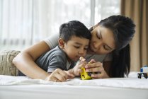 Asiático madre e hijo jugando con juguetes en la cama - foto de stock