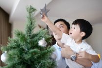 Happy young asian father and son decorating fir tree — Stock Photo