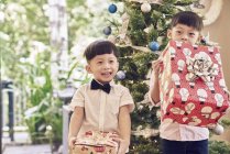 Happy boys holding christmas gifts neat fir tree — Stock Photo