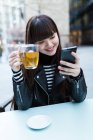 Jovem atraente asiático mulher no cidade usando smartphone e tendo chá — Fotografia de Stock