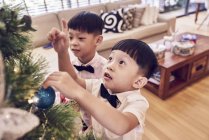 Happy young asian boys celebrating christmas together and decorating fir tree — Stock Photo