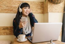 Молода приваблива азіатська жінка використовує смартфон у кафе — стокове фото