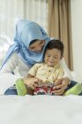 Молода азіатська мусульманська мати і дитина розважаються вдома з іграшками — стокове фото