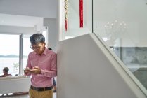 ВІДПОВІДЬ азіатського чоловіка в окулярах, користуючись вдома смартфоном. — стокове фото