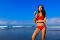 Asiatique fille sur une plage en bikini avec une crème glacée dans sa main . — Photo de stock