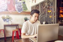 Happy young asian man working with laptop in bar — Stock Photo