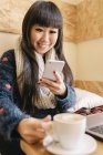 Молода приваблива азіатська жінка використовує смартфон у кафе — стокове фото