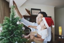 Щасливий азіатський батько і син прикрашають ялинку вдома — стокове фото