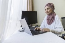 Femme musulmane travaillant à la maison avec un ordinateur portable — Photo de stock
