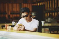 Молодий привабливий азіатський чоловік використовує смартфон у кафе — стокове фото