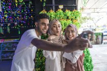 Um grupo de amigos tirando uma selfie contra as decorações hari raya . — Fotografia de Stock