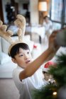 Glücklicher asiatischer Junge feiert Weihnachten zu Hause und schmückt Tannenbaum — Stockfoto