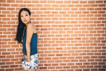 Cheveux longs asiatique femme posant sur brique mur — Photo de stock
