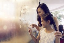 Молода азіатська жінка і дівчина малюють на склі в торговому центрі — стокове фото