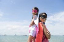 Joven asiático madre con lindo hija en superhéroe trajes posando contra azul cielo - foto de stock