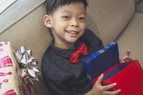 Um menino feliz com uma camisa azul abre seus presentes de Natal — Fotografia de Stock